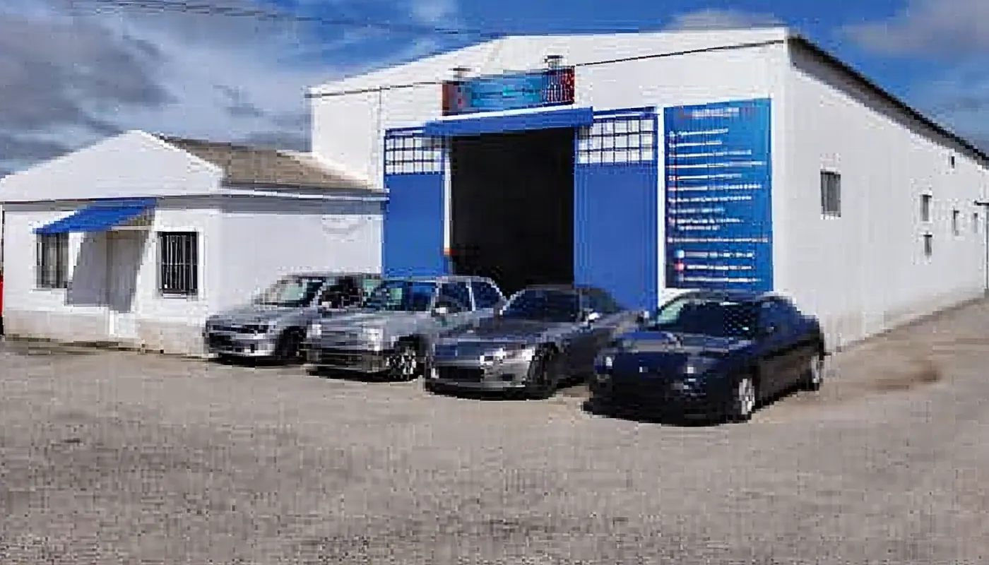 Pavilhão da oficina visto de lado, com carros à porta